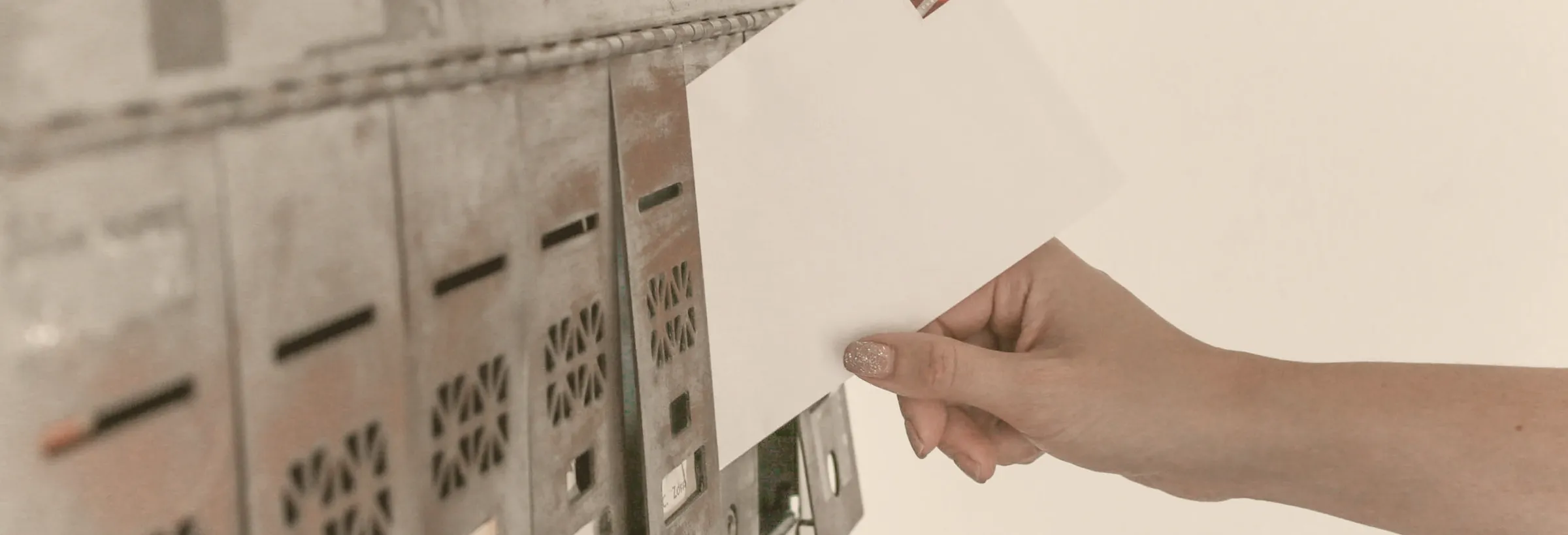 Hand wirft einen frankierten Brief in eine Briefkastenanlage