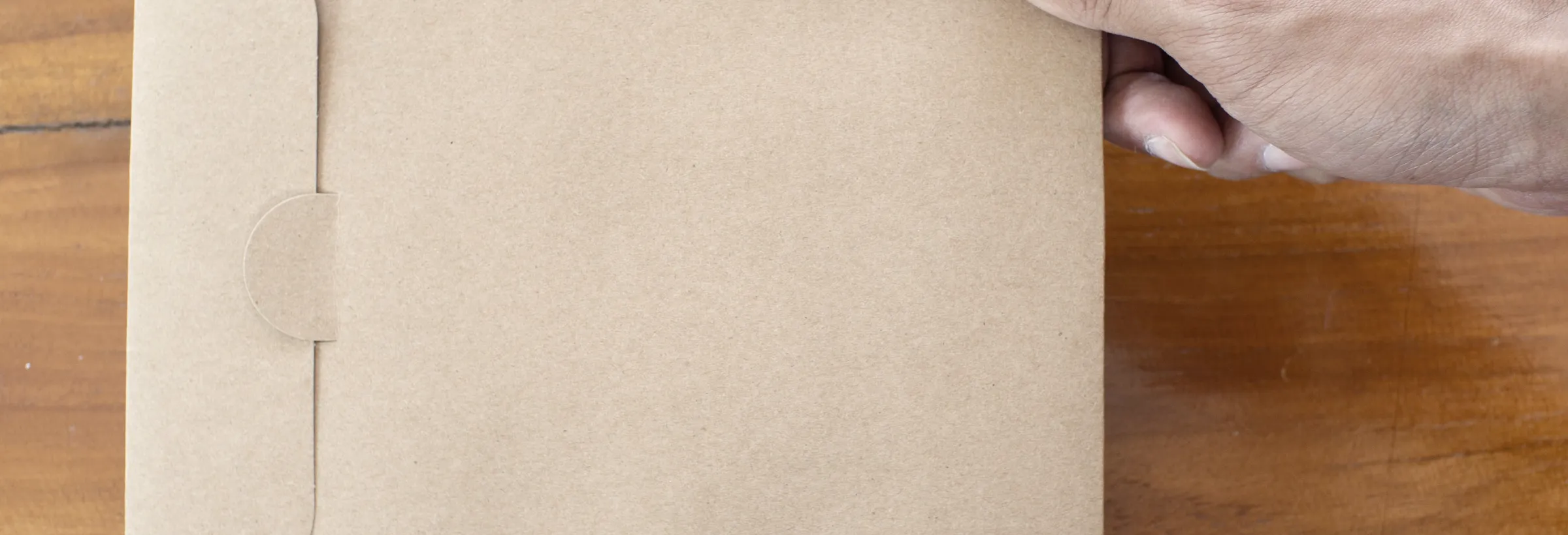 Hand hält einen Kraftpapier-Umschlag über einer Holztischplatte