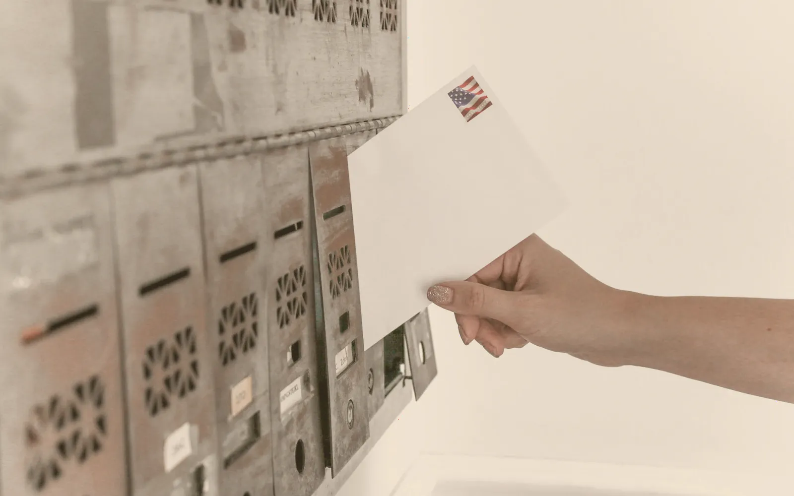 Hand wirft einen frankierten Brief in eine Briefkastenanlage