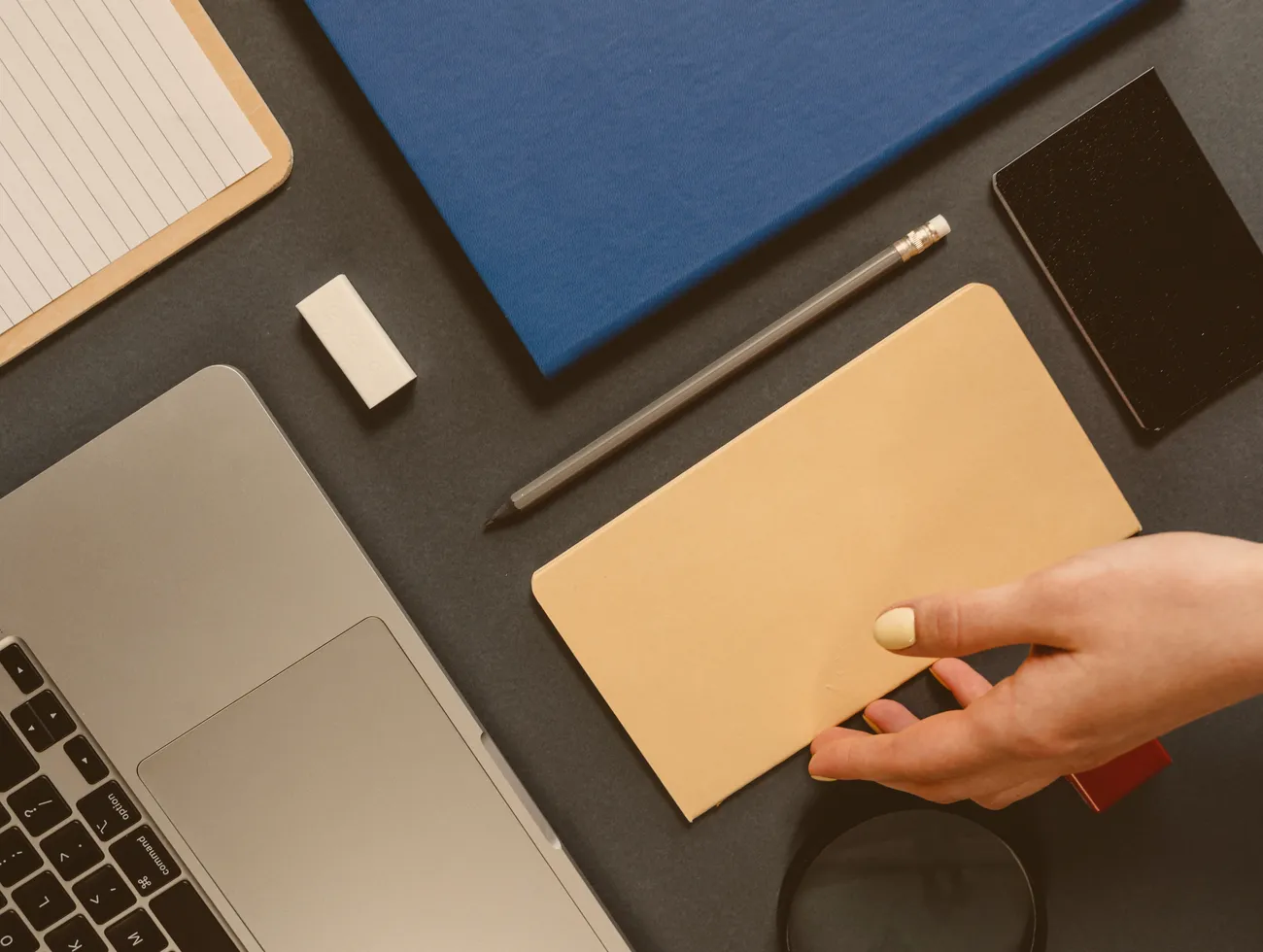 Schreibtisch von oben: eine Hand greift einen Kraftpapier-Umschlag neben einem Laptop