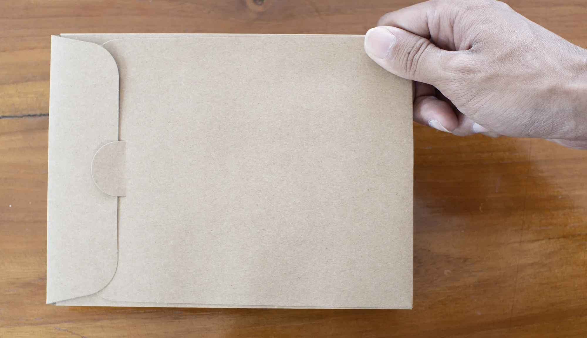 Hand hält einen Kraftpapier-Umschlag über einer Holztischplatte